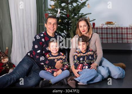 Eltern und zwei Kinder feiern weihnachten und lächeln zusammen in festlichen Pullis Stockfoto