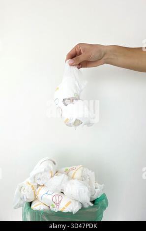 Die Hand wirft gebrauchte Windeln in den vollen Papierkorb. Stockfoto