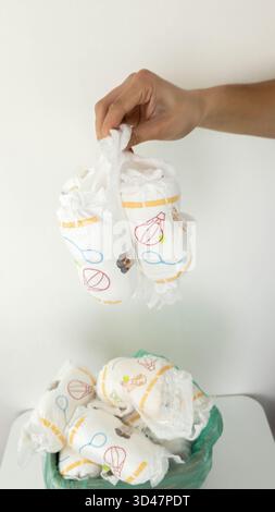 Die Hand wirft gebrauchte Windeln in den vollen Papierkorb. Stockfoto