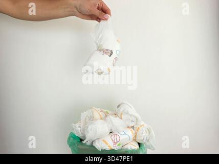 Die Hand wirft gebrauchte Windeln in den vollen Papierkorb. Stockfoto