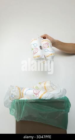 Die Hand wirft gebrauchte Windeln in den vollen Papierkorb. Stockfoto