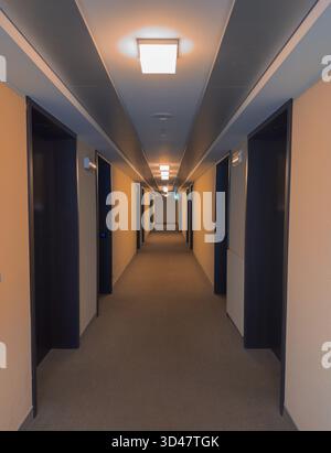 Moderner Hotelflur mit warmen Lichtern und offenen Zimmertüren Stockfoto