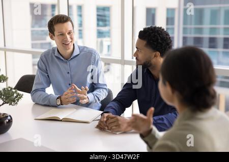 Ein lächelnder Mitarbeiter spricht mit verschiedenen Kollegen Stockfoto
