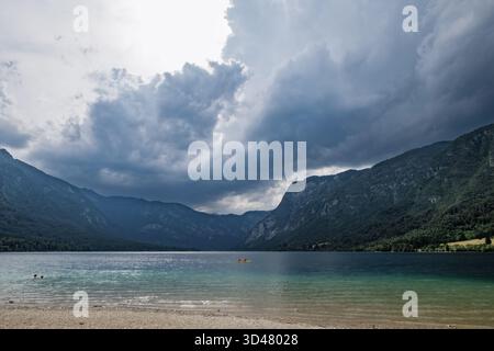 An einem dramatischen Sommertag im Triglav-Nationalpark sammeln sich Sturmwolken über dem Bohinj-See in Slowenien mit den Julischen Alpen im Hintergrund. Stockfoto