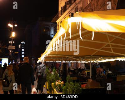 Außencafé-Sonnenschirm mit gelben Lichtern dekoriert, die in der Abenddunkel der Hauptstraße Kiew Chreshchatyk mit Piedestrains leuchten Stockfoto