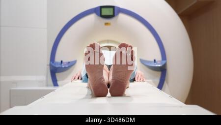 Nicht erkennbare Patientin, die barfuß auf dem Bett eines modernen MRT-Geräts liegt, bevor sie eine Untersuchung durchläuft Stockfoto