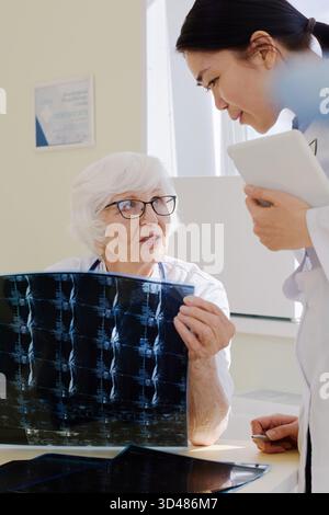 Reife Arztpraxis mit junger Assistentin bei der Röntgenuntersuchung des Patienten nach MRT-Verfahren im Krankenhaus Stockfoto