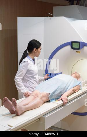 Ärztin steht bei der älteren Frau auf einem beweglichen Bett und macht sich auf die MRT-Untersuchung in der modernen Klinik vorbereitet Stockfoto