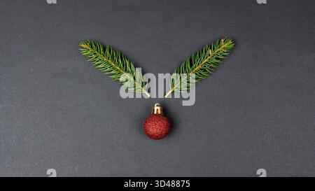 Rentierkonzept mit Tannenzweigen und roter Weihnachtskugeldekoration auf schwarzem Papierhintergrund Stockfoto