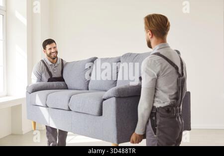 Serviceteam, zwei Männer mit großem Sofa, bewegten Möbel, arbeiteten zusammen, lächelten, zogen um Stockfoto