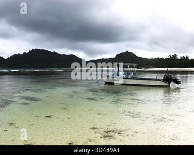 Kleines Fischerboot, das auf ruhigem Meerwasser in der Nähe des Sandstrandes und der Küste unter stimmungsvollem Himmel schwimmt. Friedliche Küstenlandschaft mit Gelassenheit. Stockfoto