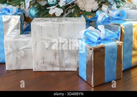 Elegant gewickelte Geschenke, Geschenkboxen werden unter einem geschmückten Weihnachtsbaum platziert, der mit blauen und silbernen Ornamenten verziert ist, um fröhliche Feiertage zu schaffen Stockfoto