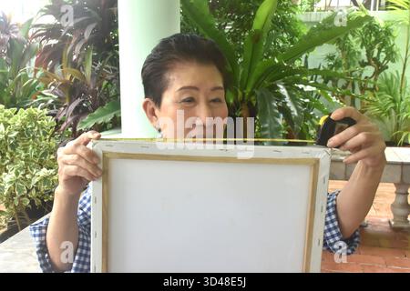 Asain ältere Frau misst Leinwandbild-Rahmen im Vorhof zu Hause Stockfoto