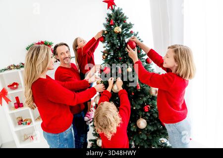 Eine fröhliche Familie versammelt sich, um einen Weihnachtsbaum drinnen zu dekorieren, um Wärme und Zweisamkeit in dieser Weihnachtszeit zu schaffen Stockfoto