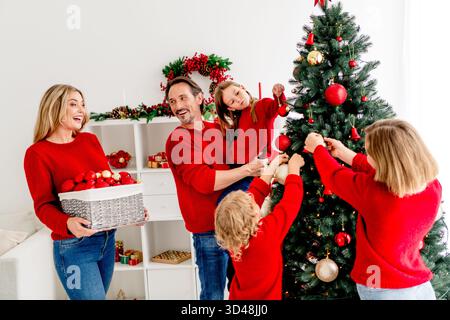 Familienmitglieder zu Hause schmücken den Weihnachtsbaum gemeinsam in einer gemütlichen Weihnachtsszene Eltern Kinder und Freunde in Pullover teilen Freude Stockfoto