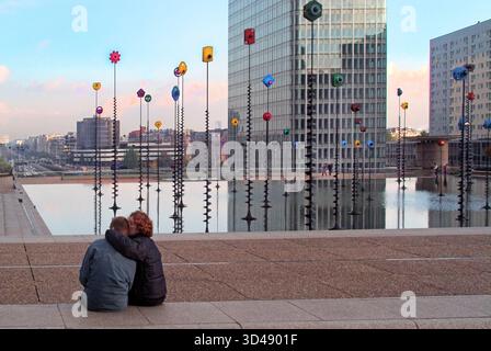 Archivszene aus dem Jahr 2003 in Paris ein Hochhaus mit Blick auf einen unbekannten freundlichen Mann und ein Ehepaar, das allein neben dem fast verlassenen und friedlichen Takis Basin sitzt, dieses Signaux-Lumineux-Kunstwerk, das von Griechenland entworfen wurde der Künstler Panayiotis Vassilakis, das Paar, das vielleicht die Beleuchtung auf den Pfählen beobachtet, die in der Stilllage und im flachen Boden gepflanzt wurden Wasser mit den Lichtern an den Stangen, die in der Dämmerung über dem La Défense Business Park zum Leben erwachen im Departement Hauts-de-seine in Paris Frankreich EU Stockfoto