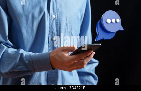 Der Mann hält ein Telefon mit einer digitalen Chat-Blase oben, die für Kommunikation, soziale Netzwerke und Messaging steht Stockfoto