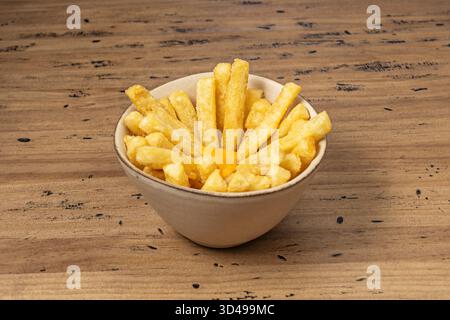 Die seitliche Beleuchtung unterstreicht die knusprige, sprudelnde Textur dieser traditionellen Pommes Frites und schafft Schatten, die ihre unregelmäßige, rustikale Form betonen Stockfoto