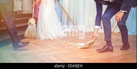 Die Braut und der Bräutigam fegen feierlich die Fliesen der zerbrochenen Platte. Traditionelles slowakisches Hochzeitsritual Stockfoto
