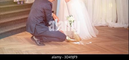 Die Braut und der Bräutigam fegen feierlich die Fliesen der zerbrochenen Platte. Traditionelles slowakisches Hochzeitsritual Stockfoto