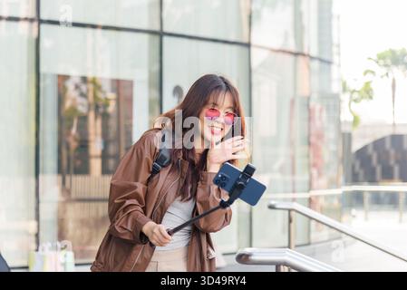 Asiatische Frau, Mode-Lifestyle-Bloggerin, lächelt hell, vloggt vor dem Einkaufszentrum, kreiert Stockfoto