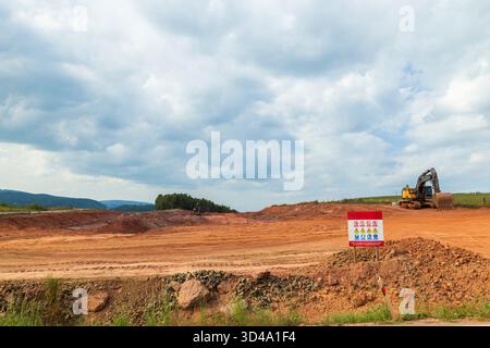 Erdbewegungsmaschinen, die roten Boden auf einer sich entwickelnden Baustelle Formen Stockfoto