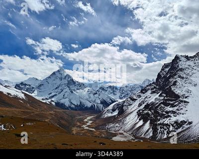 Schneebedeckte Gipfel erheben sich über ein riesiges Tal mit felsigen Hängen und dynamischen Wolkenformationen. Nepal, Himalaya Stockfoto
