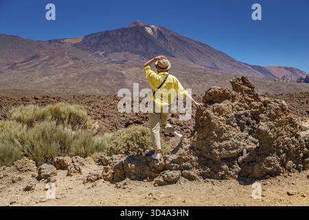 Ein einsamer Reisender steht still, fasziniert von der vulkanischen Schönheit des Teide auf Teneriffa, gekleidet in einem leuchtend gelben Hemd und Strohhut Stockfoto