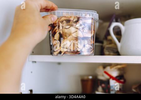 Die Hand der Frau stellt eine Plastikkiste mit Apfelchips auf das Regal. Sachgerechte Lagerung von Produkten in versiegelten Vakuum-Kunststoffkästen Stockfoto