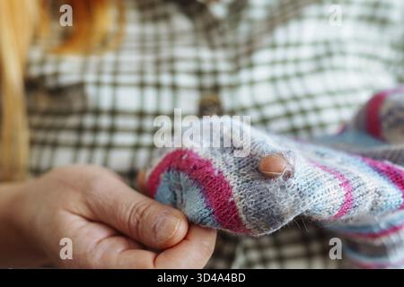 Frau zeigt ausgefranste, gerissene Löcher in einer alten Wollsocke Stockfoto