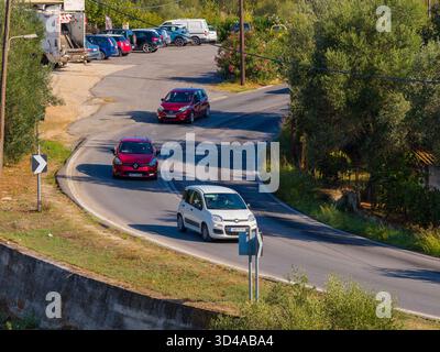 Die Drohne nahm drei Autos auf, darunter ein weißer Fiat und zwei rote Autos, die entlang einer scharfen S-Kurve auf einer sonnigen Landstraße fuhren Stockfoto
