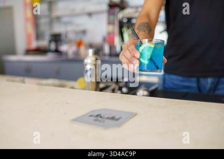 Crema, Italien - 25. August 2025 ein erfahrener Mixologe bereitet in einer modernen Bar einen leuchtend blauen Cocktail zu, garniert mit frischer Zitrone und Strohhalm Stockfoto