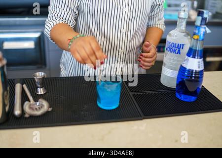 Crema, Italien - 25. August 2025 Ein Barkeeper bereitet an einer belebten Bar einen lebhaften blauen Cocktail zu, der klare Spirituosen und farbenfrohe Liköre kombiniert Stockfoto