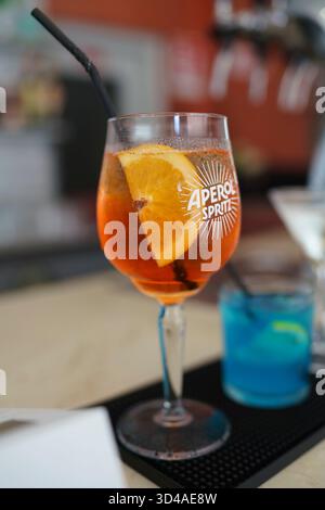 Crema, Italien - 25. August 2025 erfrischender Orangencocktail mit einer Zitrusscheibe und einem dunklen Strohhalm, serviert in einem stielförmigen Glas mit verschwommenem Hintergrund Stockfoto