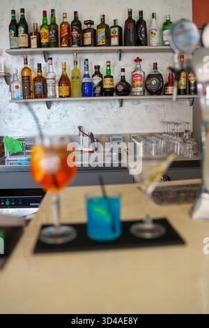 Crema, Italien - 25. August 2025 zwei bunte Cocktails, serviert an einem Bartheken mit einem Regal mit Spirituosenflaschen im Hintergrund, ein erfrischendes Getränk Stockfoto