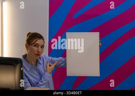 Frau, die auf ein weißes Blatt im Büro zeigt. Der Mitarbeiter gibt Gesten, um die Leinwand an der Theke im hellen Servicebereich zu leeren Stockfoto