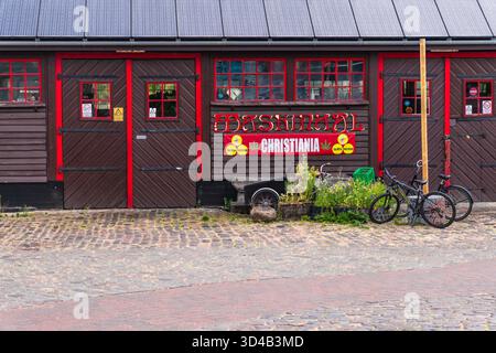 Rustikale Holzfassade des Gebäudes in Freetown Christiania, Kopenhagen, mit CHRISTIANIA auf rotem Banner mit Cannabisblättern-Symbolen, Fahrräder geparkt Stockfoto