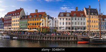 Farbenfrohe Fassaden entlang des Nyhavn Ufers mit entspannenden Menschen in Restaurants im Freien und historischen Booten im Kanal. Kopenhagen, Dänemark Stockfoto