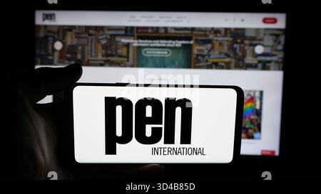 Stuttgart, Deutschland - 10-31-2025: Person mit Handy mit Logo des Schriftstellerverbandes PEN International auf dem Bildschirm vor der Webseite. Stockfoto