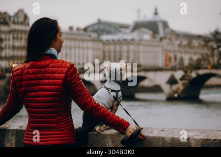 Paris, Frankreich 8. Oktober 2024 Frau in roter Jacke mit einem kleinen Yorkshire Terrierhund am Fluss. Reise-Lifestyle mit Haustier, Stadtbesichtigung, Begleiter Stockfoto