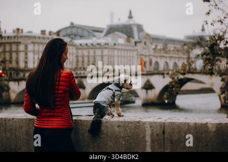 Paris, Frankreich 8. Oktober 2024 Frau in roter Jacke mit einem kleinen Yorkshire Terrierhund am Fluss. Reise-Lifestyle mit Haustier, Stadtbesichtigung, Begleiter Stockfoto