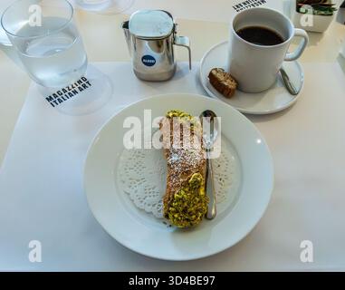 Cold Spring, NY - US - 8. November 2025 Ein reichhaltiges Café Americano und Pistazien-Cannoli werden elegant auf einem weißen Tisch im Café Silvia im Magazzi serviert Stockfoto