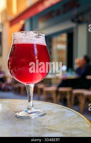 Ein Glas Himbeer-lambic-Bier in einem Restaurant im Freien mit verschwommenen Gebäuden in der Altstadt oder Vieille Ville in Nizza, Südfrankreich Stockfoto