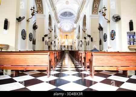 Das sonnendurchflutete Innere einer großen Kirche verfügt über eine hohe gewölbte Decke, verzierte Dekorationen und lange Holzbänke. Stockfoto