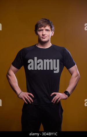 Ein selbstbewusster junger Mann in schwarzer Sportbekleidung, der seine Fitness und Energie präsentiert Stockfoto