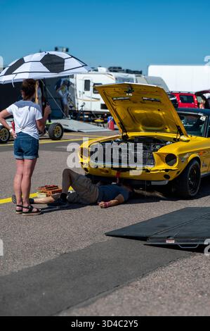Gelber Oldtimer Mit Geöffneter Motorhaube Auf Der Car Show, Mechaniker Arbeiten Am Motor, Während Zuschauer Uhren Sehen Stockfoto