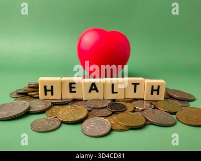 Das Bild zeigt einen roten Herzschlag und das Wort GESUNDHEIT mit Buchstabensteinen, die alle auf einem Stapel Münzen liegen. Stockfoto