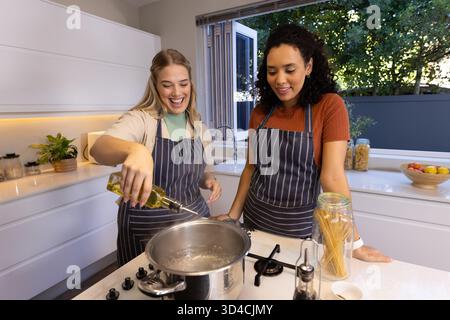 Olivenöl gießen, verschiedene weibliche Freunde kochen auf Kücheninsel, mit Topf auf Gasherd Stockfoto