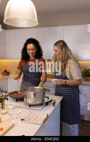 Kochen Sie verschiedene weibliche Freunde mit Tomatensoße auf der modernen Kücheninsel mit einer Olivenölflasche Stockfoto