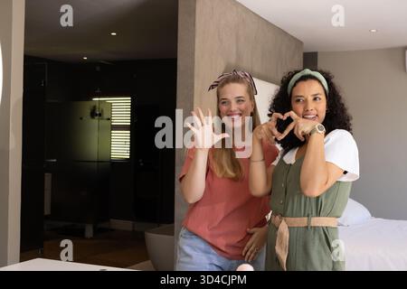 Lächelnde, vielfältige Freundinnen posieren neben der Wand des Schlafzimmers mit eingebautem Kosmetikbereich im Bad Stockfoto